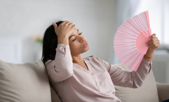 Woman feeling hot, fanning herself with a handheld fan.
