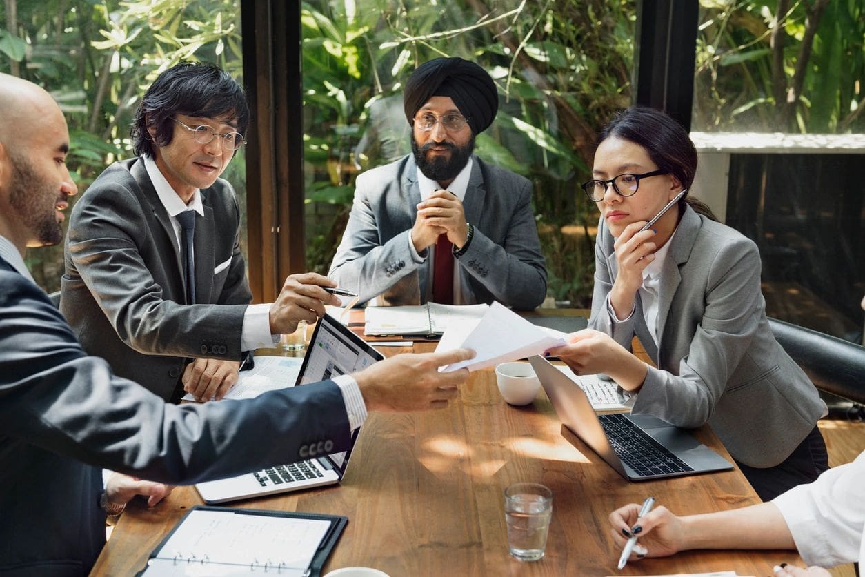 Diverse professionals collaborating around a table with documents and laptops.